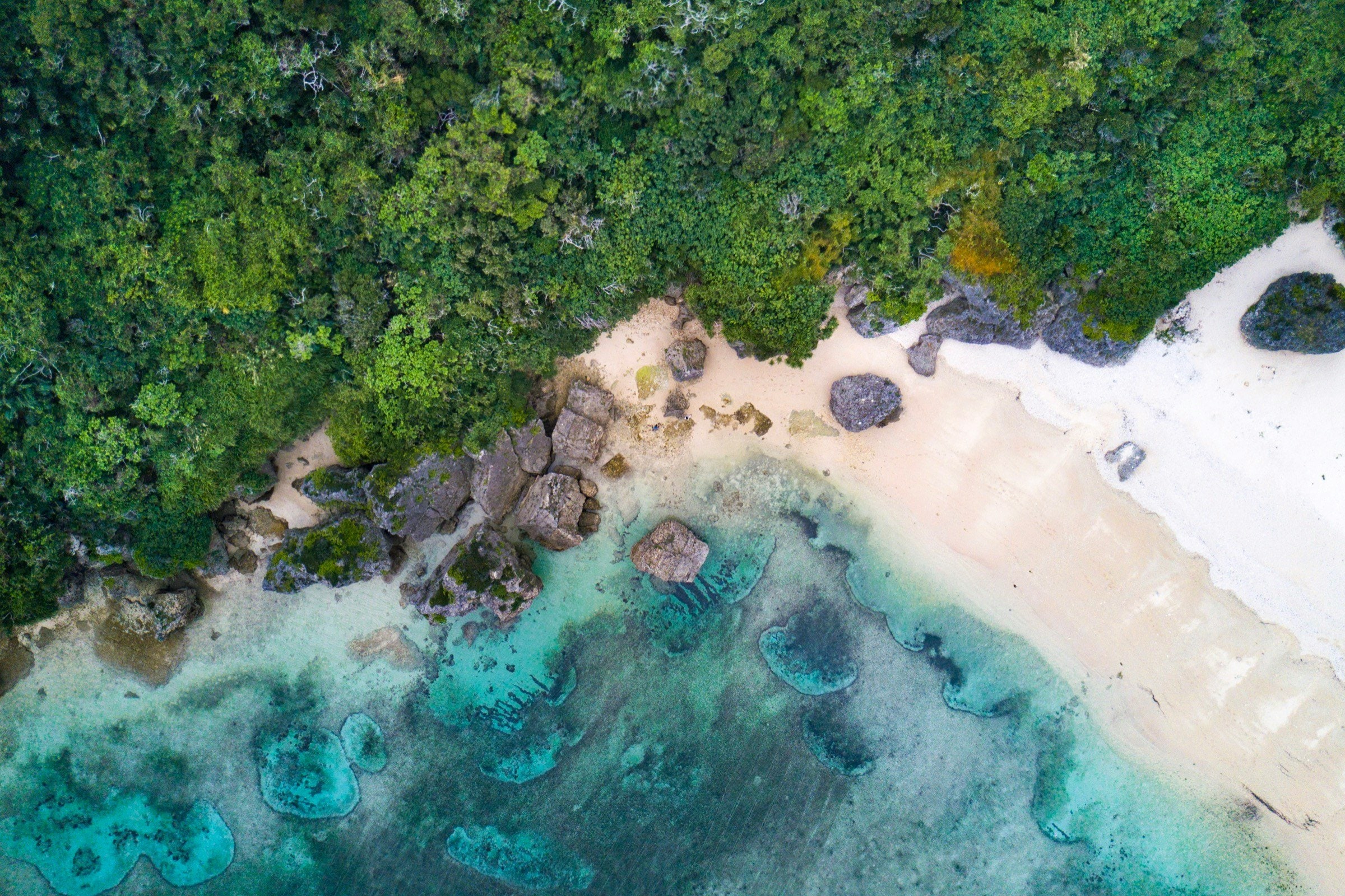 A reef beach from above, boulders in turquoise water — photo by Ryo Yoshitake, Unsplash